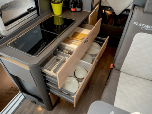 KNAUS BOXLIFE PLATINUM SELECTION 2027 – Küche mit Stauraum Küchenzeile im KNAUS BOXLIFE PLATINUM SELECTION 2027 mit Kochfeld und geöffneten Schubladen für Besteck und Geschirr